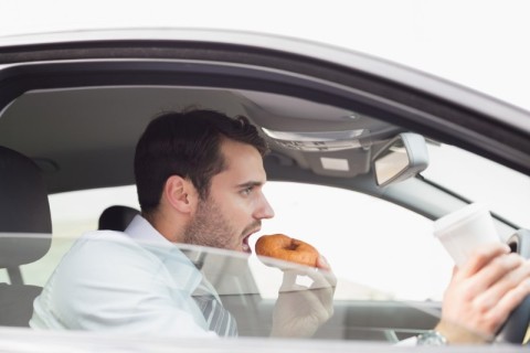 man eating a donut and drinking a coffee while driving