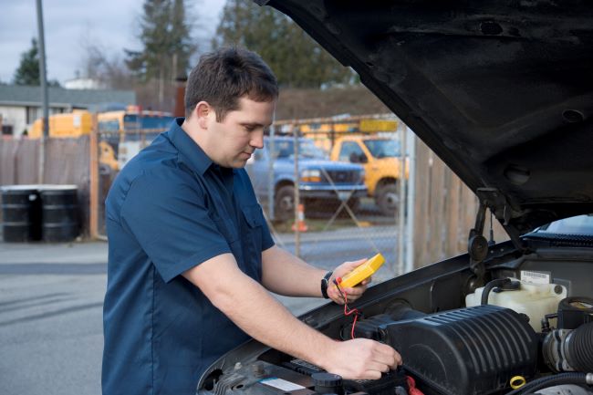 a man in a blue shirt tests his trucks battery with a yellow device