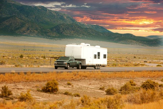 a black truck towing a white rv drives through the desert scenery during the sunset